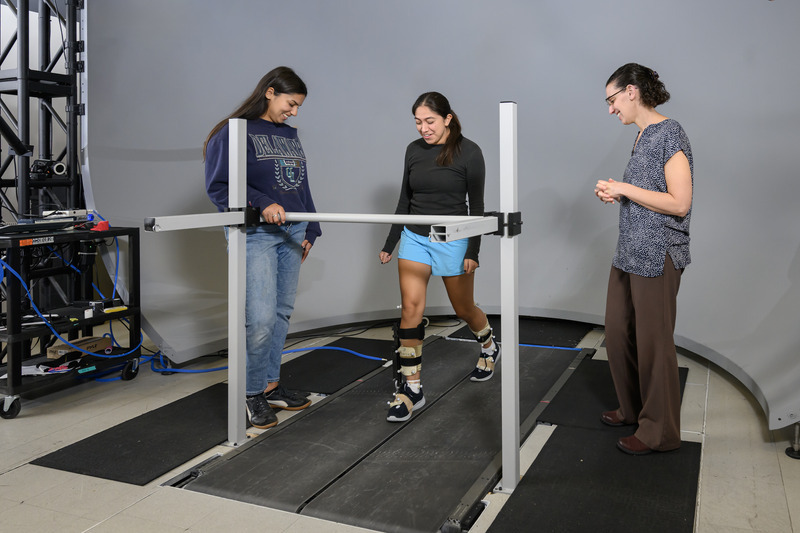Iris Sanchez, a senior mechanical engineering major, walks on a split-belt treadmill to demonstrate how an ankle-foot orthosis (AFO) can be used to control load on the tendon in people recovering from Achilles tendinopathy. Sanchez works in the lab alongside mentors Elisa Arch (right), associate professor of kinesiology and applied physiology, and biomechanics and movement science doctoral student Zahra McKee, who are pioneering this research.